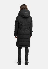 Zwarte pufferjas met een getailleerde taille, grote capuchon en gevoerde textuur. Draag het over donker slim-fit broeken en enkellaarsjes.