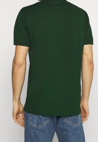 Polo shirt vert foncé à manches courtes, avec un col plat et un ourlet droit. Porté avec un jean en denim bleu.