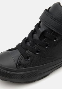 Černé vysoké tenisky s texturovaným koženým povrchem, gumovou špičkou, černými tkaničkami a polstrovaným límcem. Obsahují kovové průchodky a vzorovanou podrážku.