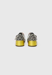 Black and white patterned shoes with medium golden block heels, smooth leather finish, rounded toe, and black accents on the upper.
