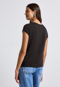 Zwarte top met korte mouwen en een ronde halslijn, met een gladde textuur en een iets getailleerd ontwerp. Gecombineerd met lichtblauwe jeans.
