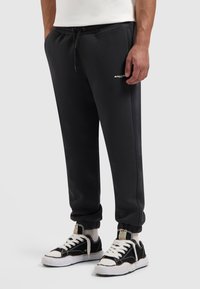 Zwarte joggingbroek met elastische boorden en een tailleband met trekkoord, voorzien van een klein wit logo. Gecombineerd met zwart-witte sneakers.