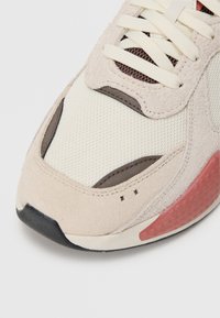Jasno beżowe sneakersy z siateczkową cholewką, zamszowymi akcentami i ciemną gumową podeszwą. Ciekawy czerwony detal na pięcie z teksturowanym wzorem.