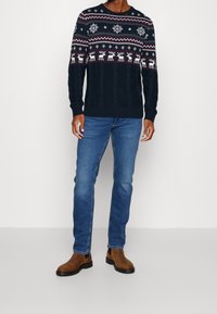 Marinblå tröja med julsymboler, prydd med vita snöflingor och renar. Paret med blå jeans och bruna ankelstövlar.