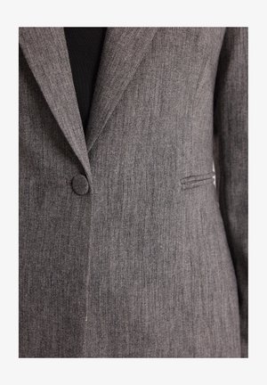 Szary żakiet o teksturowanej powierzchni, z pojedynczym zapięciem na guzik, wyciętymi klapami i detalem bocznej kieszeni.