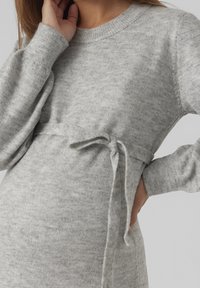 Grå stickad klänning med lös passform, långa ärmar och midjeband. Den mjuka texturen och det subtila mönstret ger ett bekvämt utseende.