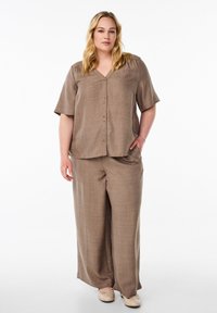 Relaxed-fit, short-sleeve shirt and wide-leg pants in a textured light brown fabric with buttons. Simple, neutral footwear completes the outfit.