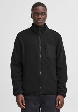 Giacca in pile nera con zip e colletto alto, chiusura frontale con zip e tasca sul petto. Presenta tasche laterali e maniche lunghe.