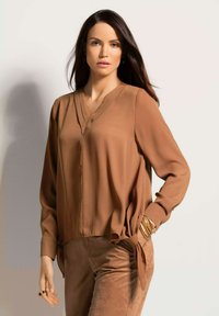 Braune, leichte Bluse mit V-Ausschnitt und langen Ärmeln, die eine lockere Passform und seitliche Bindungen aufweist. Glatte Textur, minimalistisches Design.