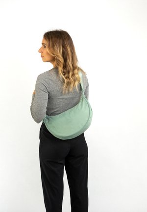 Borsa a spalla verde in nylon indossata a tracolla, con una forma curva, texture liscia e tracolla regolabile. Design semplice e minimalista.