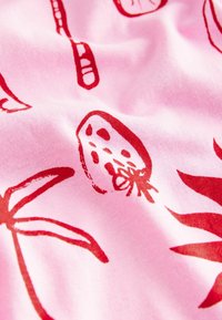 Cotton fabric in light pink with red tropical fruit and leaf patterns. The texture appears smooth and slightly stretchy.