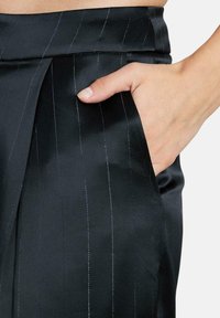 Zwarte stoffen broek met een gladde textuur, voorzien van fijne verticale streepjes, een zijzak en een getailleerde pasvorm bij de taille.