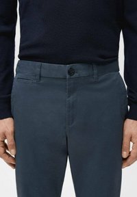 Close-up of a person wearing dark navy pants and a black long-sleeve shirt, showing button and belt loops on the pants.