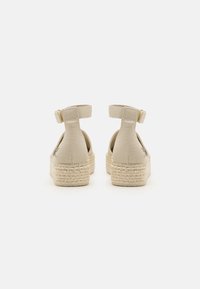 Beige espadrille sandaalit nilkkavöillä, köysikudosvälipohjilla ja sileällä kangaspinnalla. Avoin kantadesign, minimimäärä metallikoristeita.