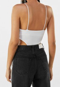 Vit ribbad crop top med tunna axelremmar, parat med högmidjade svarta denimjeans med bakfickor och en synlig etikett.