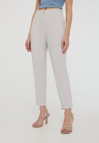 Pantaloni grigi chiari su misura con vita alta, tasche frontali e dettagli di cucitura verticale. Indossati con tacchi beige con cinturini.
