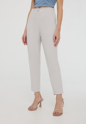 Pantaloni grigi chiari su misura con vita alta, tasche frontali e dettagli di cucitura verticale. Indossati con tacchi beige con cinturini.