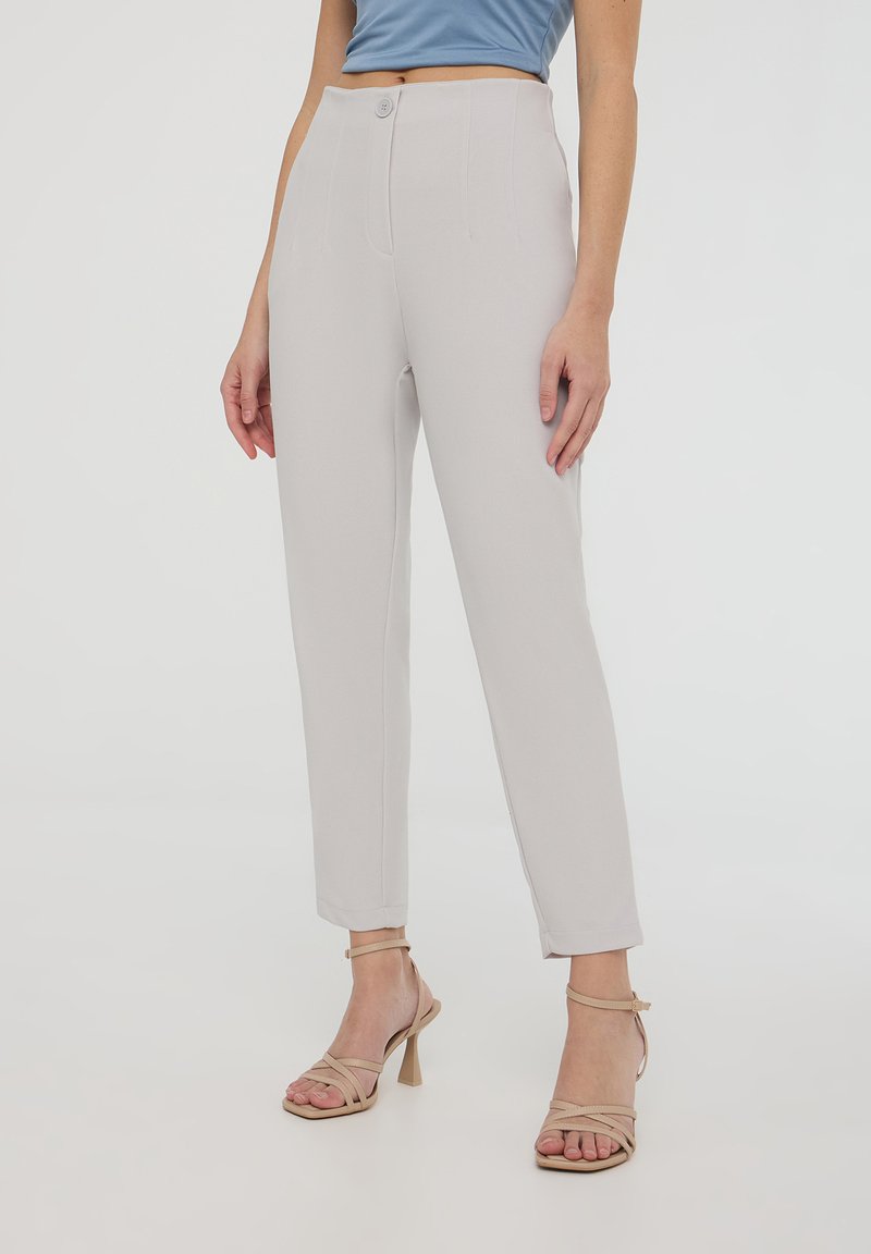 Pantaloni grigi chiari su misura con vita alta, tasche frontali e dettagli di cucitura verticale. Indossati con tacchi beige con cinturini.