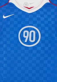 Sinine ruudustikuga Nike jersai, millel on ümmargune kaelus, featuring valge ringikujuline logo, mille keskel on "90" ja punased aktsendid kaeluses.