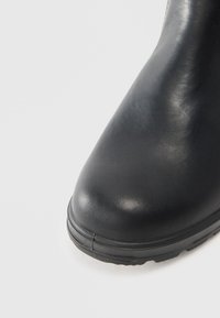 Botte en cuir noir à bout arrondi, surface texturée et semelle en caoutchouc. Présente une finition lisse et des détails de couture minimaux.