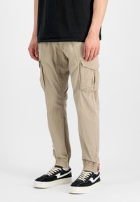 Bež hissane hlače z elastičnimi manšeti, več stranskimi žepi in sproščenim krojem. Ujemajo se z črnimi in belimi športnimi copati.