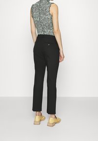 Černé přizpůsobené kalhoty s dvěma zadními kapsami a žlutou botou s vrstveným dřevěným podpatkem, doplněné texturovaným zeleno-černým topem.