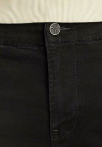 Schwarze Jeans aus Denim mit einem Metallknopf mit Brandlogo, feinen Nahtdetails und einer glatten Textur an der Taille.