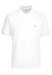 Polo en coton blanc avec une patte de boutonnage à trois boutons, manches courtes, et un petit logo brodé sur la poitrine gauche. Texture lisse.