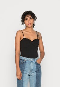 Bodysuit preto ajustado com decote franzido, combinado com jeans de denim azul de cintura alta em patchwork, apresentando tons variados e bolsos.