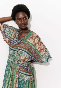 Robe multicolore avec des motifs floraux bruns, bleu-vert et verts. Coupe ample, manches courtes et taille cintrée. Tissu léger et texturé.