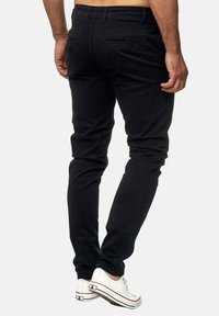 Czarne dopasowane dżinsy uszyte z elastycznego materiału, z tylnymi kieszeniami i gładką powierzchnią. W zestawie z białymi canvasowymi sneakersami.