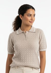 Beżowy sweter polo z krótkim rękawem o strukturze dzianiny warkoczowej, z białym kołnierzem i mankietami w paski, dwuknapowym rozcięciem i luźnym krojem.