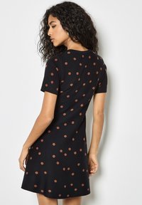 Abito nero a maniche corte con silhouette svasata e pois marroni. Tessuto morbido e scollatura rotonda, vista posteriore mostrata.