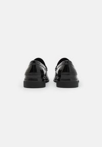 Zwarte leren schoenen met een glanzende afwerking, ronde neus, lage zwarte zool en een vouwontwerp bij de enkel. Zichtbare stiksels accentueren.