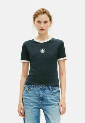 Zwarte T-shirt met witte afwerking, voorzien van een klein grafisch embleem op de borst. In combinatie met lichtblauwe denim jeans. Eenvoudig ontwerp.
