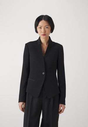 Blazer nero su misura realizzato in tessuto liscio, con colletto a riviera, chiusura a un bottone e due tasche frontali.