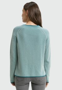 Sweter dzianinowy w jasnym turkusie z pionowymi paskami. Posiada okrągły dekolt, długie rękawy i ribbowany dół. Teksturowany, miękki materiał.