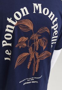 Marineblå bomull T-skjorte med et brunt botanisk trykk og teksten "Le Ponton Montpellier" samt merkevare detaljer nederst.