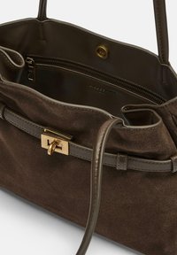 Brązowa zamszowa torebka z złotymi elementami, wyposażona w zamykane na zamek wnętrze oraz regulowany pasek na ramię. Miękka faktura i dobrze zarysowany kształt.