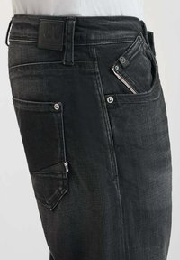 Jeans en denim noir avec une coupe droite, cinq poches et une finition texturée. Comprend une étiquette en cuir à la taille et des coutures contrastées.