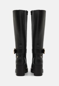 Czarne skórzane kozaki za kolano na klockowym obcasie, z zamkiem błyskawicznym oraz ozdobnym paskiem z metalowym, złotym akcentem.