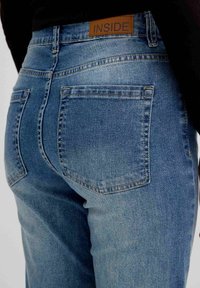 Jeans de mezclilla de color azul claro con una cintura alta, que cuentan con un parche de cuero marrón etiquetado como "INSIDE" en la parte posterior y dos bolsillos traseros.