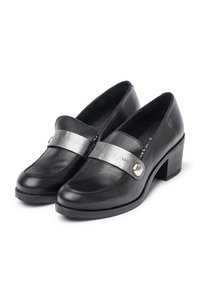 Mocasines de cuero negro con una correa metálica plateada, punta redonda y tacón cuadrado. Presentan un botón decorativo plateado en la correa.