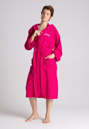 Accappatoio fucsia in tessuto asciugamano, dotato di cappuccio e cintura, con due tasche frontali e testo ricamato sul petto.