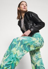 Jaqueta de couro preta, blusa cinza, e calças flare com padrão de mármore verde, apresentando tons ondulados de verde e azul. Textura suave.