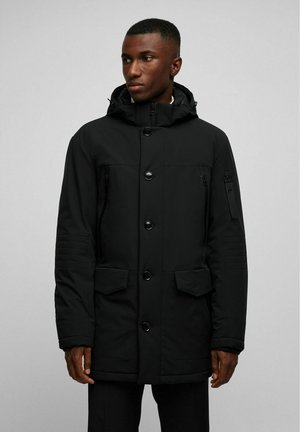 Zwarte gewatteerde parka jas met een capuchon, een knoopsluiting aan de voorkant, een ritszak op de borst en twee grote voorzakken met getextureerde mouwaccenten.