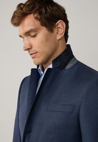Marineblaue Jacke mit passgenauer Schnittführung, ausgestattet mit einem strukturierten grauen Kragen und einer Brusttasche, aus glattem Stoff gefertigt.