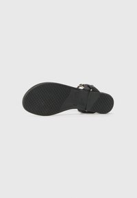 Suela de sandalia negra con superficie de goma texturizada. Presenta una tira ancha y una hebilla ajustable para un ajuste seguro.