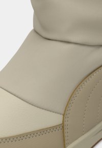 Lichtbeige sneaker met een gladde, matte textuur, gestikte accenten, een ronde neus en een iets verhoogde enkellijn.