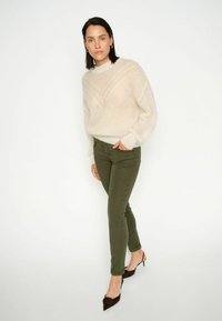 Kremowy, dziergany sweter z geometrycznymi wzorami, zestawiony z oliwkowozielonymi spodniami i brązowymi szpiczastymi szpilkami. Prosty wzór, miękka faktura.